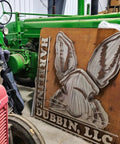Green tractor next to sign with rabbit design and 'Hareline Dubbin, LLC', in a warehouse setting