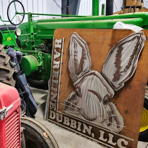 A large sign with a hare design and text reading 'Hareline Dubbin, LLC' leaning against a vintage green tractor.