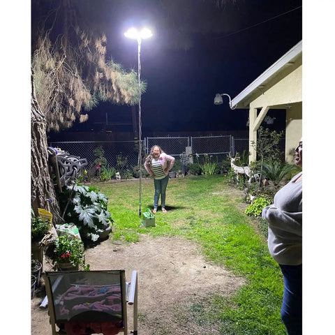 Outdoor night scene with 30,000 Lumen Telescoping Camping Light With Remote And Manual Control, illuminating a garden area.