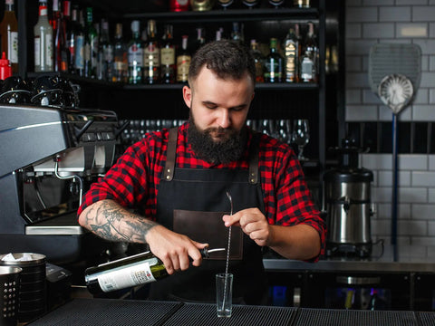 Bartender wearing Black Canvas And Leather Apron For Chefs Bartenders Baristas Barbers And Grill Masters Handmade In USA pours drink.
