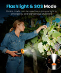 A person using an orange rechargeable outdoor camping light with remote to illuminate grape vines, showing flashlight and SOS mode.
