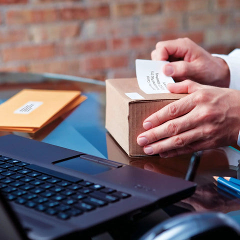 Hands applying a shipping label on a box using the No Sweat Direct Thermal Label Printer With Zero Ink Hassles.