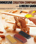 Person using Pro Grade Micro Detail Sander Kit on wooden toy airplane, sanding block and sandpaper sheets in foreground.