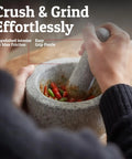Person using Heavy Duty Granite Mortar And Pestle Set Hand Carved From Natural Stone Two Cup Grinder Bowl For Fresh Guacamole Salsa Pesto Herbs And Spices Six Point Three Inches Wide Grey Great For Grinding Spices Seeds And Seasonings On The Countertop with unpolished interior for max friction.