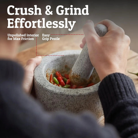 Person using Heavy Duty Granite Mortar And Pestle Set Hand Carved From Natural Stone Two Cup Grinder Bowl For Fresh Guacamole Salsa Pesto Herbs And Spices Six Point Three Inches Wide Grey Great For Grinding Spices Seeds And Seasonings On The Countertop with unpolished interior for max friction.