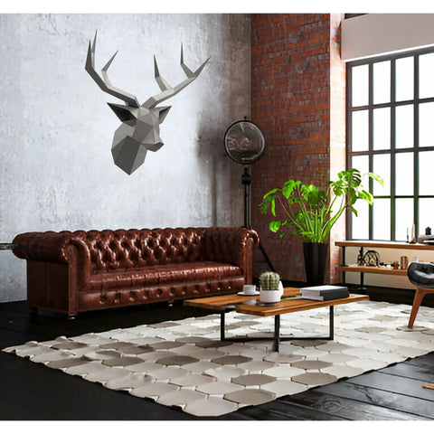 Modern living room with brown leather sofa, geometric deer head wall art, hexagonal rug, and large plant by the window.