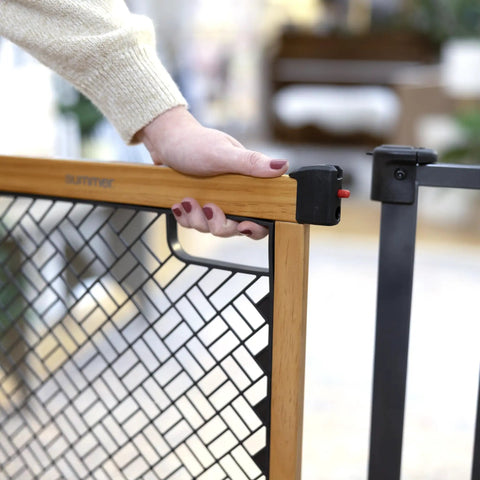 Close-up of a hand holding the solid wood cherry stain arched baby gate with charcoal gray metal frame 30 inch tall fits openings