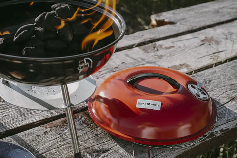 14 Inch Portable Charcoal BBQ Grill With 3 Point Locking Lid and burning coals, showcasing dual venting system, red lid on table.