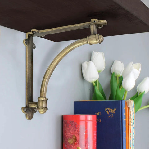 Heckin Heavy Duty Cast Iron Shelf Brackets, 2 Pack Antique Gold Wall Mounts supporting a wooden shelf with flowers and books.