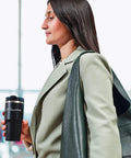 Person holding a coffee travel mug while wearing a green jacket, demonstrating the portability of the mug.