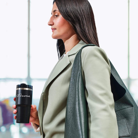 Person holding a coffee travel mug while wearing a green jacket, demonstrating the portability of the mug.