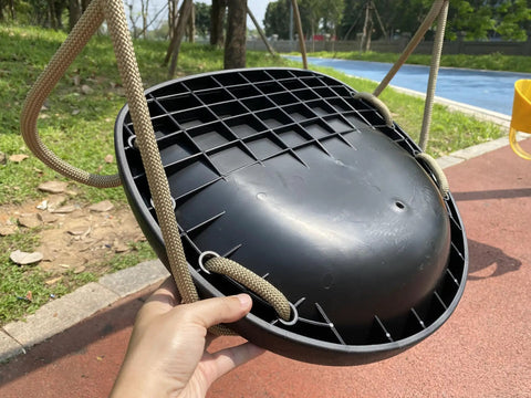 Heavy Duty Swing Seat For Adults And Kids With Weatherproof Ropes, shown close-up in black with hands, outdoor setting