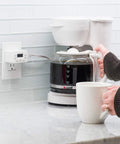 24 Hour Digital Plug Timer With One Polarized Outlet No Fuss Two Programmable On Off Cycles For Lamps And Indoor Lighting 125VAC Indoor Timer White 1 Pack Model 45184 plugged into wall beside a coffee maker.