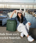 Woman sitting by marina with Underseat Carry-On Luggage With 28L Capacity, Sustainable Travel Bag Made From Recycled RPET in Juniper Green.