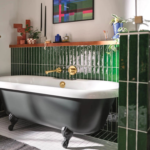 Modern bathroom with green tiles, white freestanding tub, and decorative items on shelf