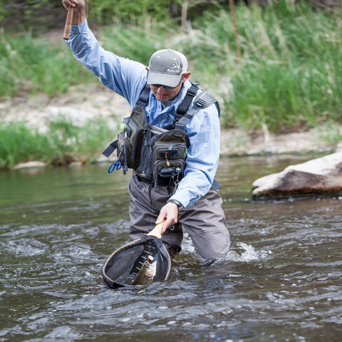 Angler wearing Ultra Lightweight Fly Fishing Vest With 14 Pockets And Front Zip Storage Olive Green in a river catching fish.