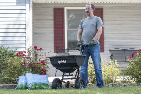Person using Pro Push Broadcast Spreader 85 Lb Capacity With Durable Plastic Hopper, Corrosion-Resistant And Made In USA for lawn care.