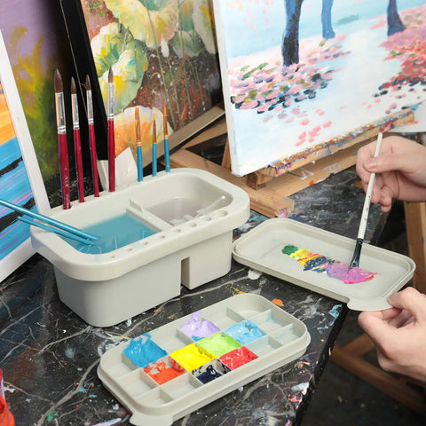 Must-Have Paint Brush Cleaner And Holder With Built-In Palette And Wash Basin For Acrylic, Watercolor, And Water-Based Paints, Compact Portable Organizer In Gray on a workspace with brushes and colorful paints.