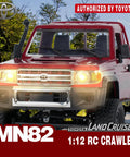 Front view of red Toyota 1/12 Scale RC Rock Crawler Pickup Truck with 2.4GHz 4WD, headlights on in a forest setting.