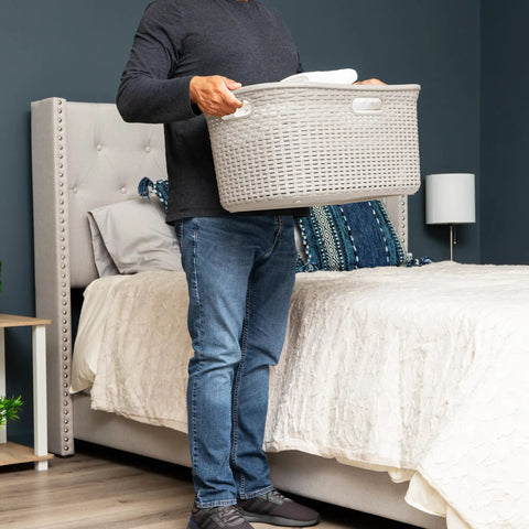 Person holding 40L Laundry Basket With Lightweight Build And Premium Wicker Look Ivory Plastic Hamper in bedroom setting