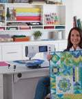 Woman holding a finished quilt near a Heavy Duty Computerized Sewing Machine With Sharp LCD Screen Quilting Kit Extension Table And Bonus Bundle.