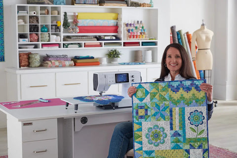 Woman holding a finished quilt near a Heavy Duty Computerized Sewing Machine With Sharp LCD Screen Quilting Kit Extension Table And Bonus Bundle.