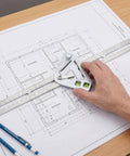 Hand using Pro Grade Stainless Steel Angle Ruler And Carpenter Square on blueprint, precise angle readings, durable for woodworking and material cutting.