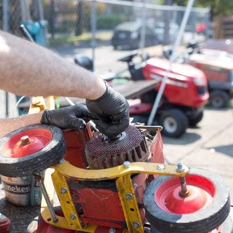 Black nitrile disposable glove on hand adjusting a red workshop machine with a circular grinding wheel