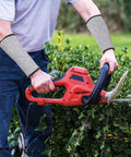 Real Deal Cut Resistant Arm Sleeves For Mechanics And Gardeners With Snug Stretch Fit Anti Puncture Forearm Guards That Make The Daily Grind A Total Breeze In Black Gray worn while using a hedge trimmer in the garden.