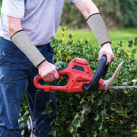 Real Deal Cut Resistant Arm Sleeves For Mechanics And Gardeners With Snug Stretch Fit Anti Puncture Forearm Guards That Make The Daily Grind A Total Breeze In Black Gray worn while using a hedge trimmer in the garden.