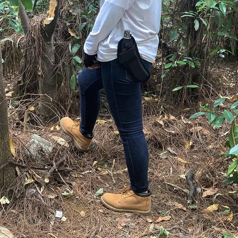 Person carrying the All-Black Sharp Edge Folding Sickle With Wooden Handle, sheath attached to belt in forest setting.