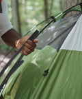 Person adjusting tent pole with green and white camping tent outdoors