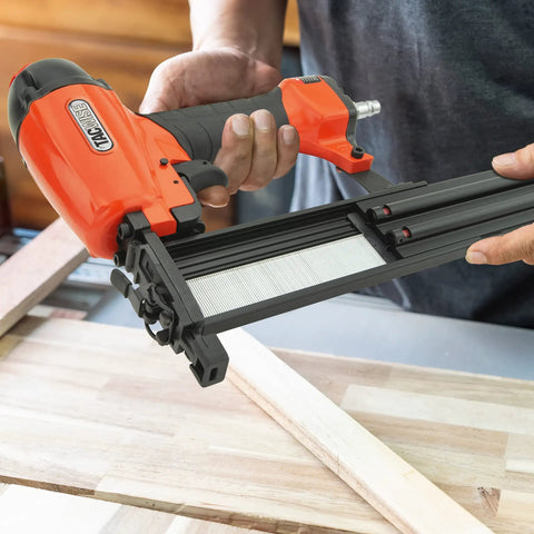 Real Deal Air Brad Nailer With Quick Release Bottom Load Magazine And 1000 18G Type 180 Brads To Knock Out Woodworking Projects In Bold Orange Carry Case held over wooden boards.