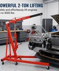 Hella Solid Heavy Duty Folding Engine Hoist And Portable Cherry Picker Shop Crane With Adjustable Boom lifting an engine in a garage.