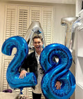 Person holding Deep Navy Blue Number 2 Balloon, 40 Inch Giant Digit Balloon For Birthday Backdrop alongside other digit balloons.