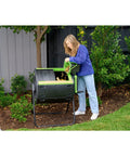 Woman using Dual Compartment 48 Gallon Compost Tumbler With Easy Turning Geared Design in a garden setting
