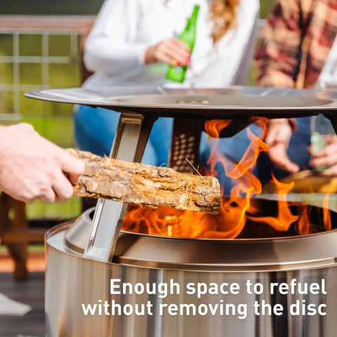 Person adding wood to fire pit with Ranger Heat Deflector Boosts Outdoor Fire Pit Warmth With Angled Design Redirecting Heat To Expand Radius