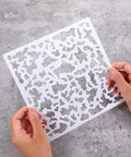 Hands holding an 8x8 inch stencil from the Six Pack Knockdown Texture Spray Stencil Kit for Drywall Repair and Plaster Walls