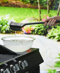 Steam Activated Grill Brush With ArmorTec Bristle Free Mesh Powered By Scrub Daddy shown being dipped in water near a grill