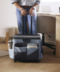 Person holding foldable utility cart with canvas organizer bag and removable saddlebag, black and grey, next to office desk