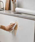 Self Adhesive Wallpaper Roll Subtle Gray Linen Texture Waterproof Vinyl Peel and Stick Film being cleaned on a cabinet surface.