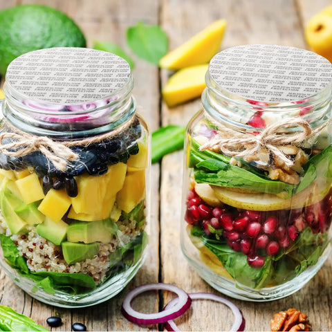 Front view: two clear glass jars with foil-sealed lids and twine, filled with layered salad ingredients.