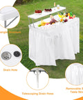 Two Tier Folding Ice Cooler Table With Skirt And Grid Rack Drain Hose Portable Party Table For Patio, Picnic, Camping And Wedding Use Keeps Drinks Cold And Food Fresh White showing features including drain hole and removable satin table skirt on grass