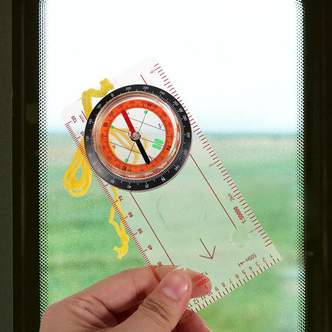 Person holding All-In-One Hiking Compass With Built-In Ruler And Navigation Tool against a window, showing detailed design.