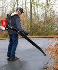 Person using Beast Gas Backpack Leaf Blower With 665 CFM And 205 MPH for leaf clearing on a driveway in a wooded area.