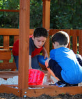 Children playing in sandbox of Skyfort II Cedar Wood Swing Set With Wave Slide, Raised Clubhouse, Kid Friendly Outdoor Playset