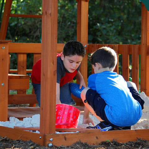 Children playing in sandbox of Skyfort II Cedar Wood Swing Set With Wave Slide, Raised Clubhouse, Kid Friendly Outdoor Playset