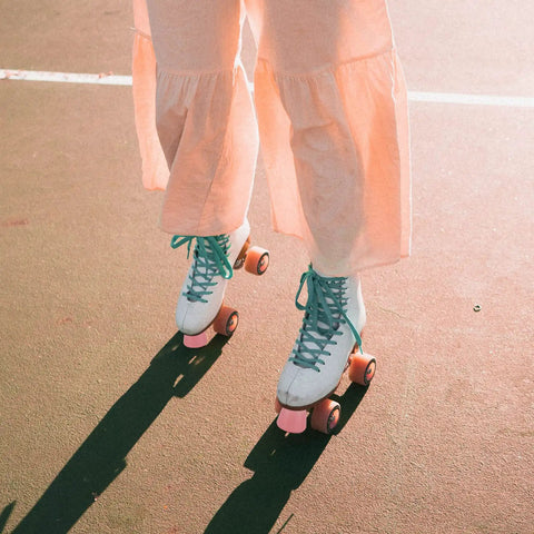 Close-up of quad skates with pink two-pack roller skate toe stoppers on feet, visible in use on outdoor pavement.