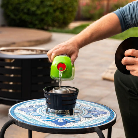 Pouring fuel into Mini Fire Pit Tabletop Torch Set Two Pack for Patio Backyard and Garden Black Metal Flame Torches.