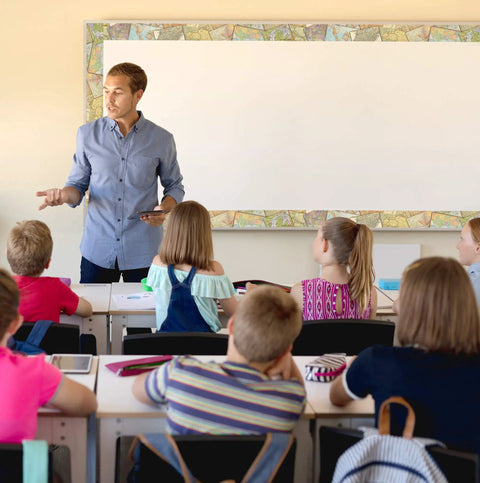Teacher in classroom with Travel The Map Straight Rolled Border Trim For Classrooms And Offices 50Ft around whiteboard